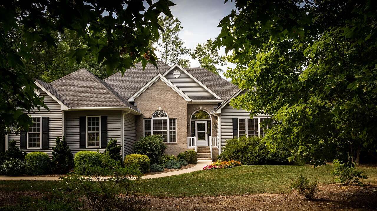 A single-story brick house with gables under mature shade trees
