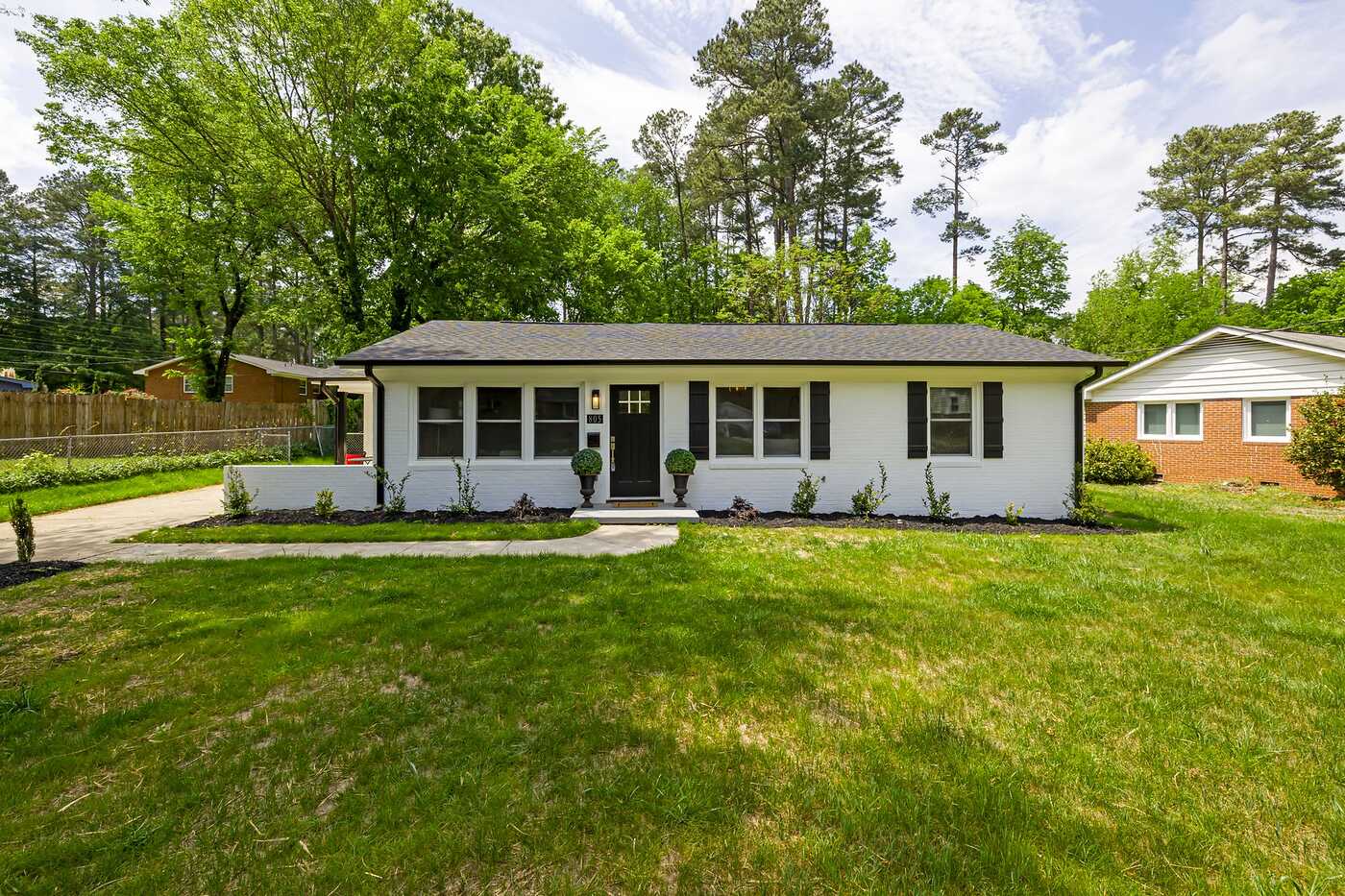 A single-story suburban house with a front lawn and trees behind it