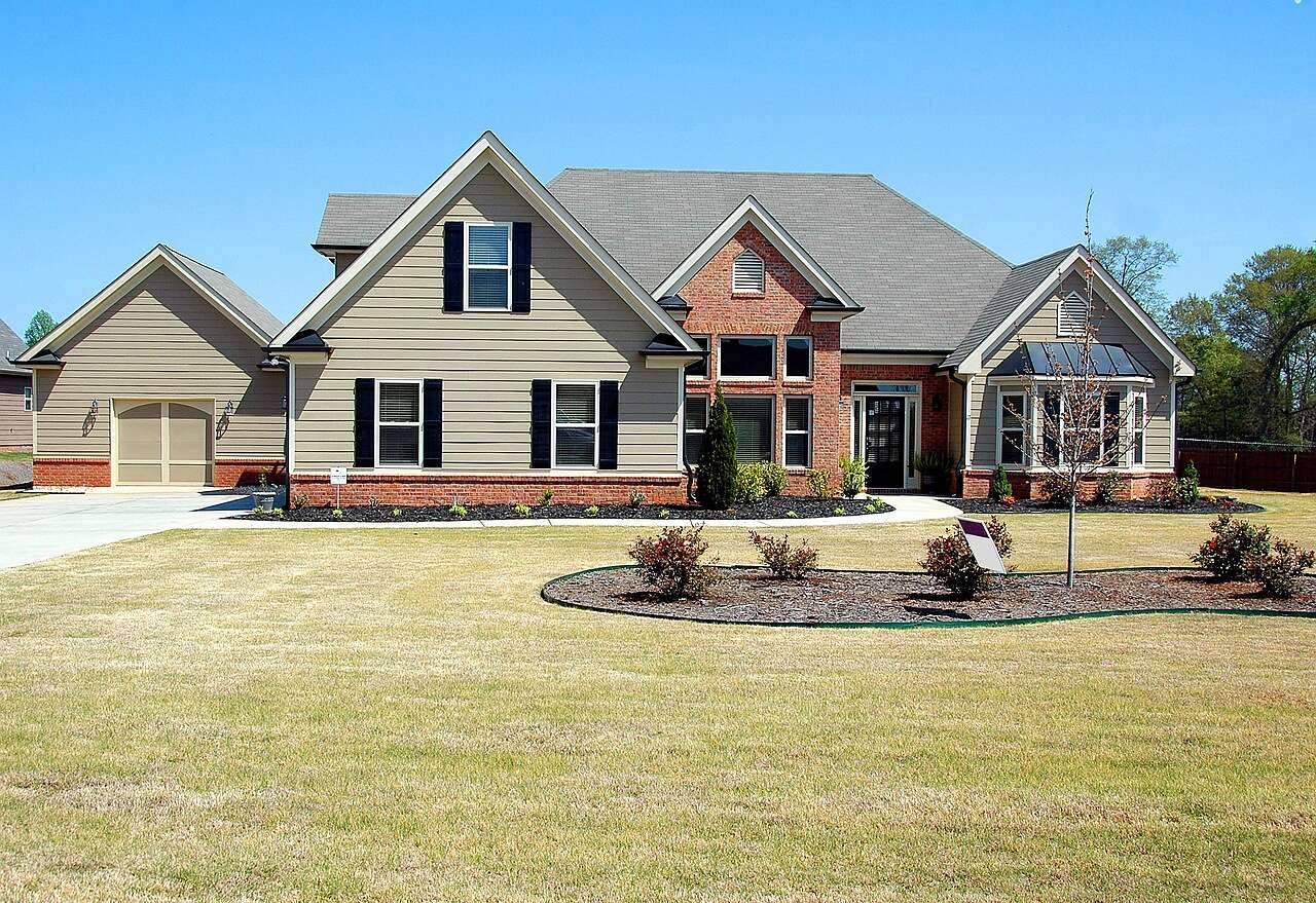 A large brick house with a landscaped front yard and trees behind