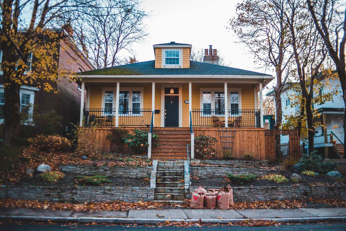 A yellow wood-frame bungalow with a front porch under bare autumn trees