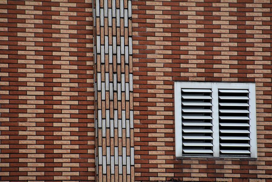 A white louvered vent set into a brick wall