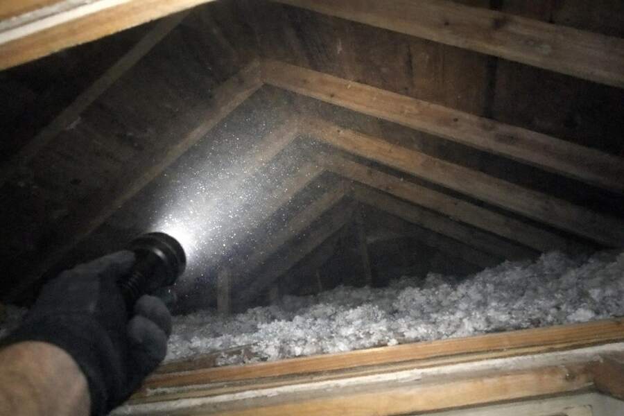 A flashlight beam sweeping the rafters of a dark attic from the hatch