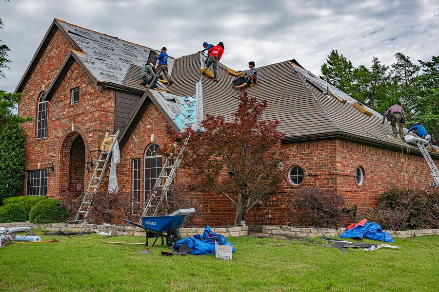 Roofers working on the steep roof of a brick house in North Texas