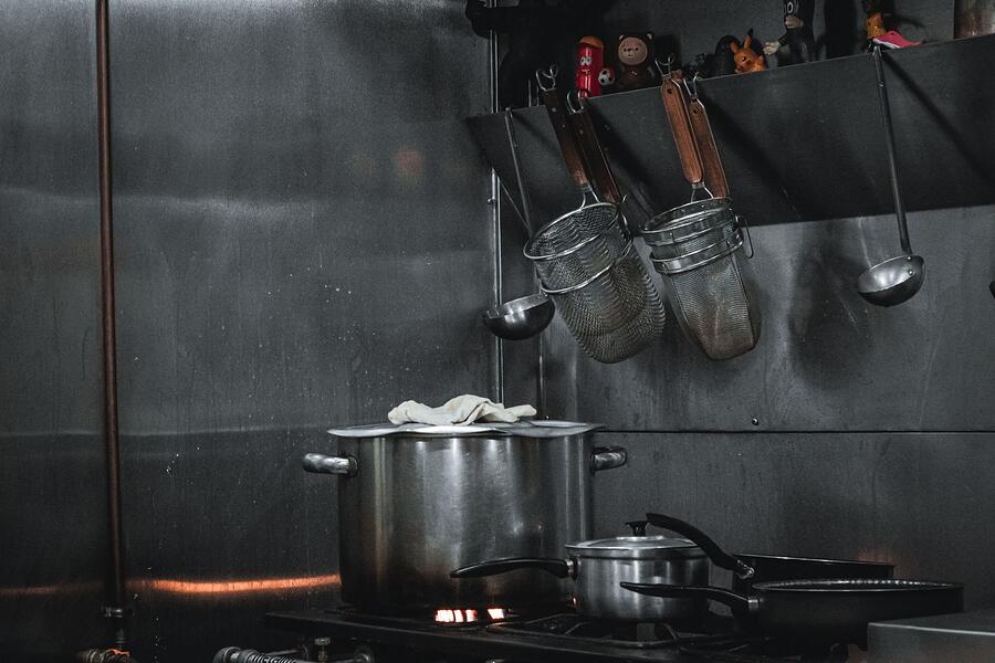 Stainless steel pots and strainers hanging over a commercial kitchen line