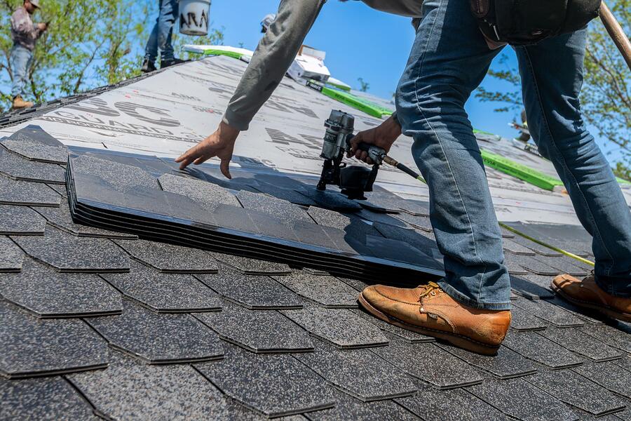 A roofer nailing new composition shingles on a residential roof